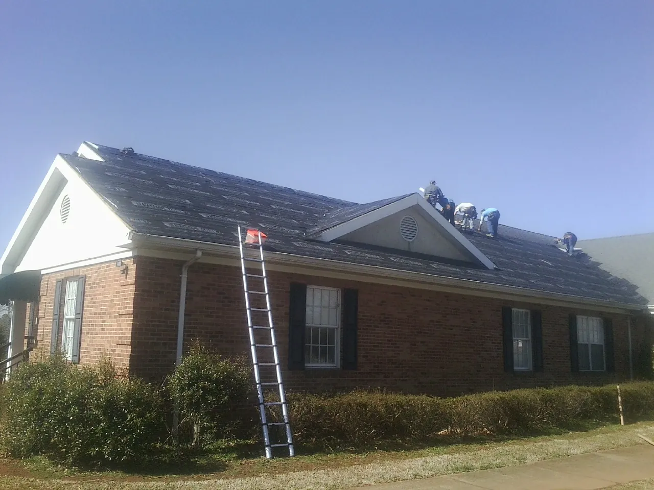Crew tearing shingles off a brick ranch roof with a ladder set — Emergency Roof Repair work by our crew in Scotia