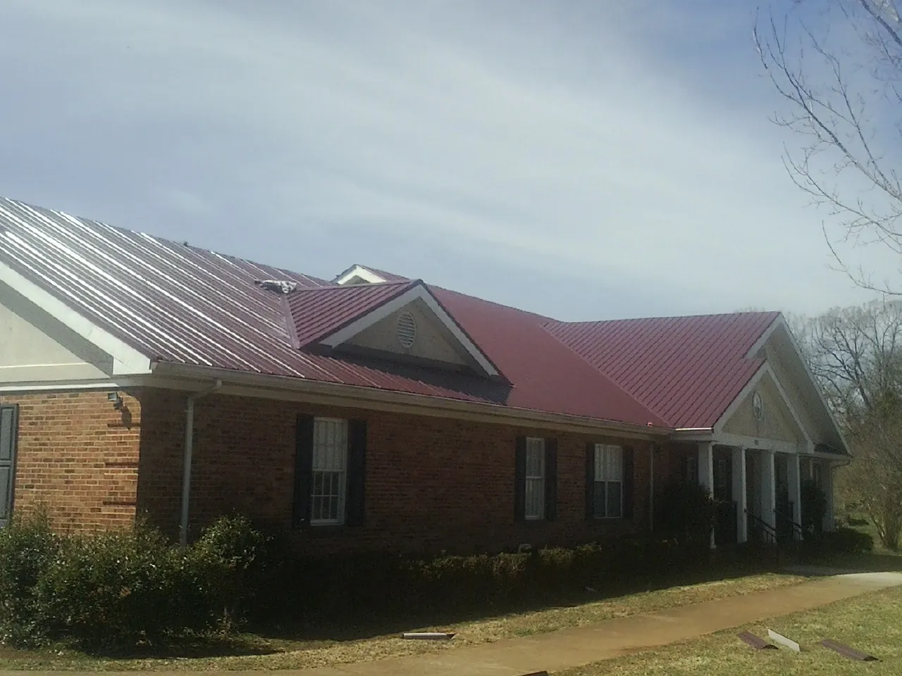 Red metal roof with gabled entries on a long brick building, from a Hail Damage Roof Repair job in Scotia