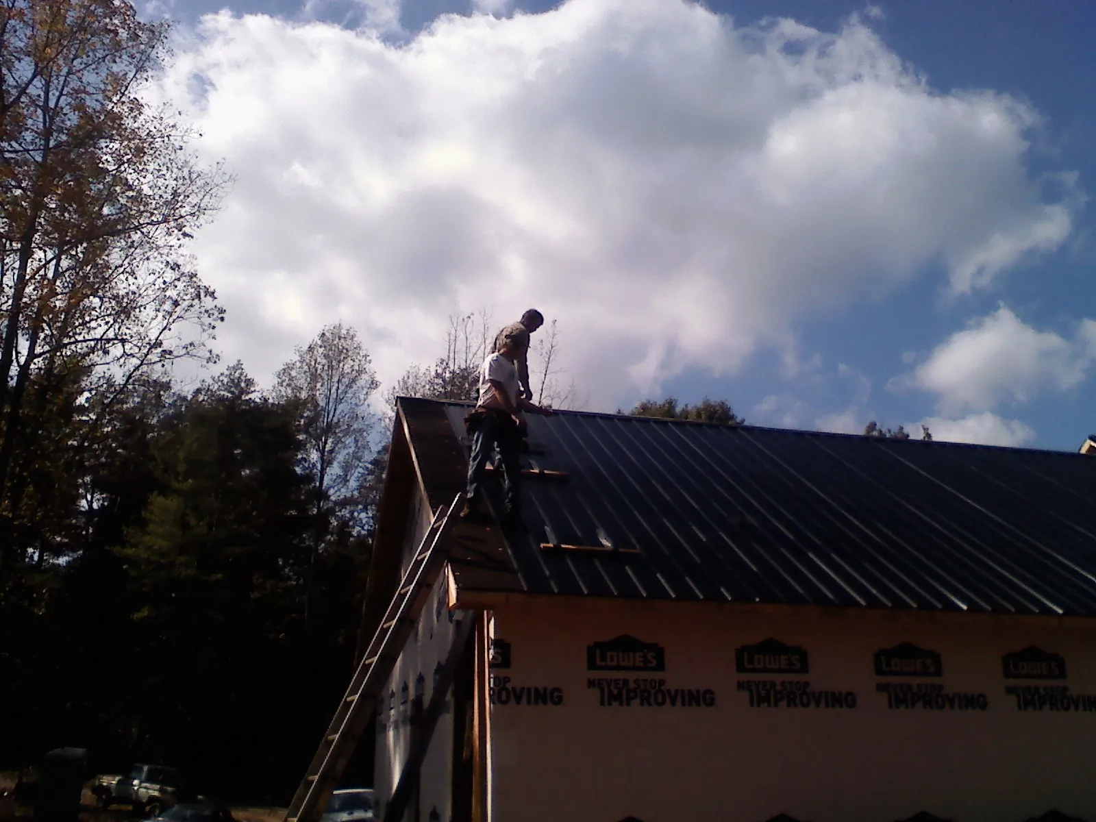 Roofer fastening dark metal panels high against a cloudy sky, from a Roof Inspection job in Scotia