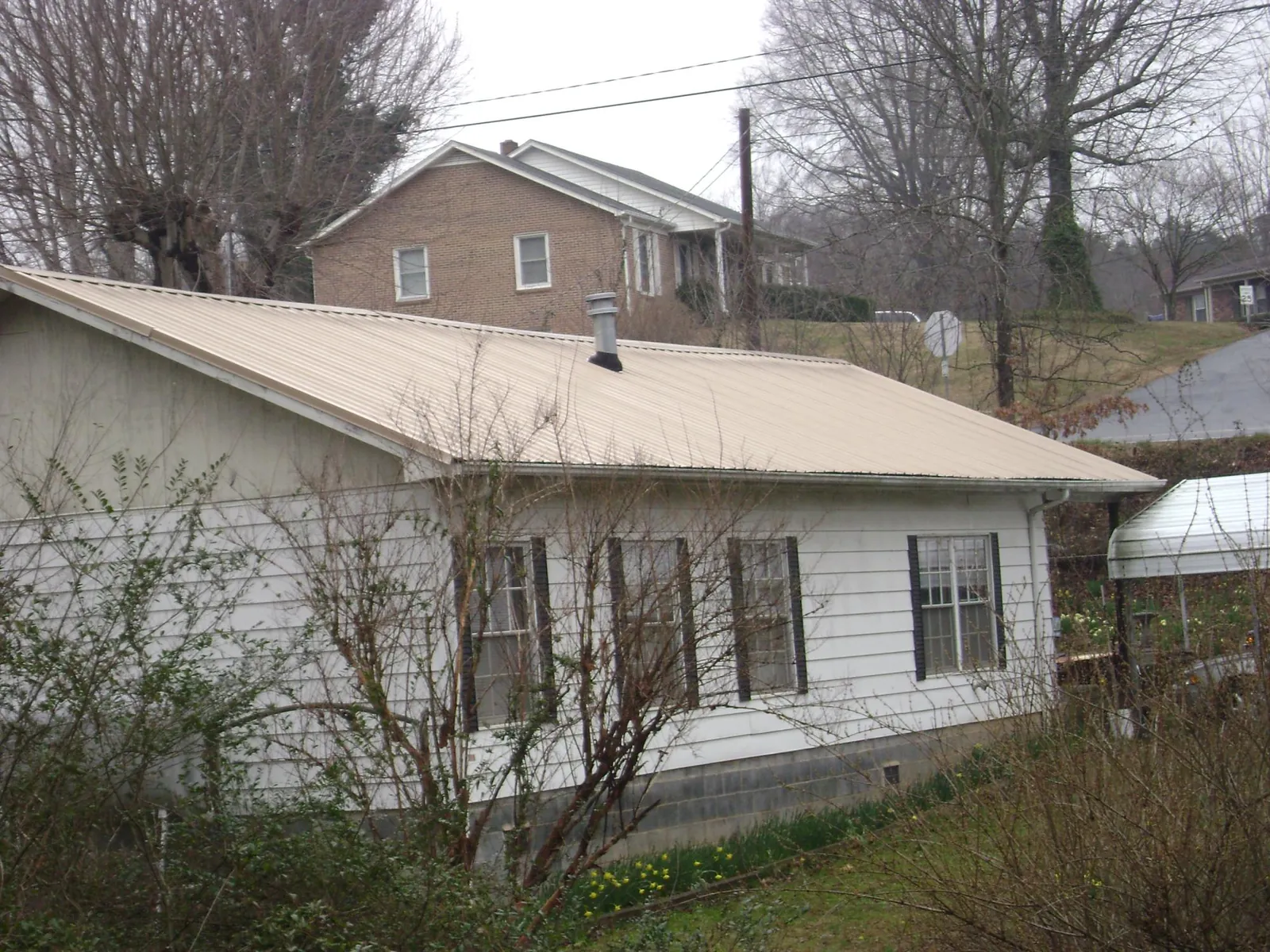 Tan metal roof on a white sided house set into a hillside — Commercial Roofing by Roofing Brothers in Scotia